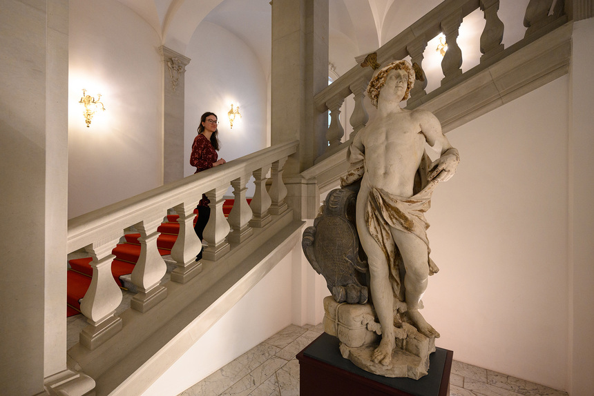 Ein FRau schaut von einer Treppe aus auf eine Männerstatue.